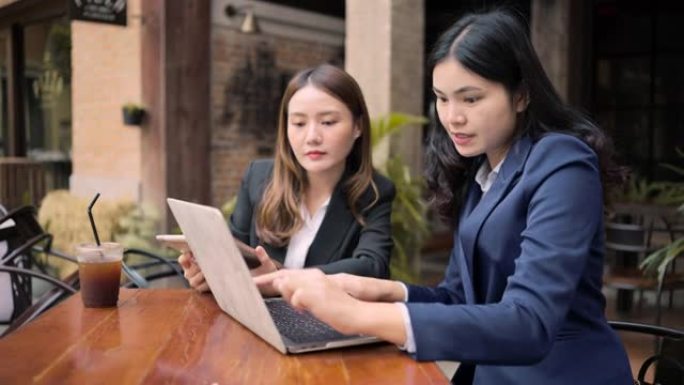 两位亚洲商界女性开会认真谈论咖啡馆外的工作。