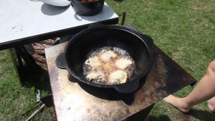 鸡大腿在沸腾的植物油中油炸。有烟和蒸汽。我们在户外用铸铁大锅做饭。