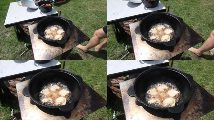 鸡大腿在沸腾的植物油中油炸。有烟和蒸汽。我们在户外用铸铁大锅做饭。