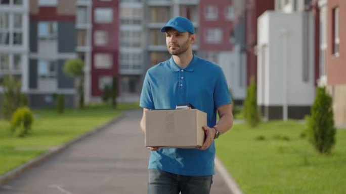 蓝色送货员在运送货物之前先将包裹发送给客户。4k分辨率和慢动作拍摄。在城市街，手里拿着包裹的男邮递员