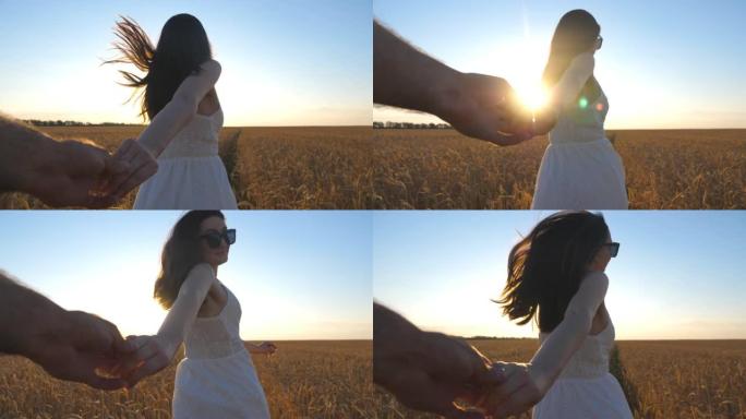 年轻女子握着男性的手，在日落背景下在无尽的麦田上奔跑。快乐的女孩带领她的男朋友沿着大麦草地。美丽的夏