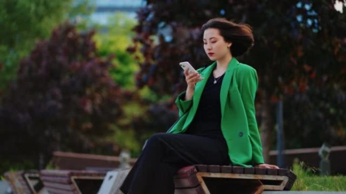 美丽的亚洲女士正在使用智能手机，在线聊天并在市中心的公园里休息