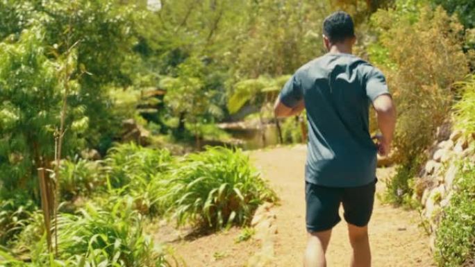 一个运动男子在沿着风景优美的小径奔跑时使用智能手表跟踪他的进度的后视图。适合男性在公园里挑战自己，专
