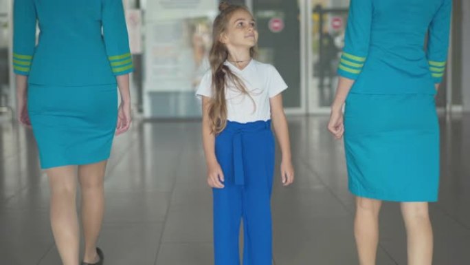 漂亮的高加索小女孩欣赏空姐进入机场，看着相机。可爱的孩子喜欢等待出国的肖像。梦想成为空姐。