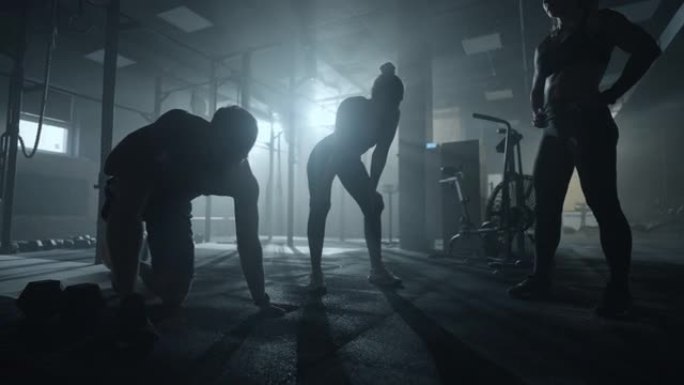 精疲力竭的健美运动员在黑暗的健身房，男女运动员的剪影，人们正在休息