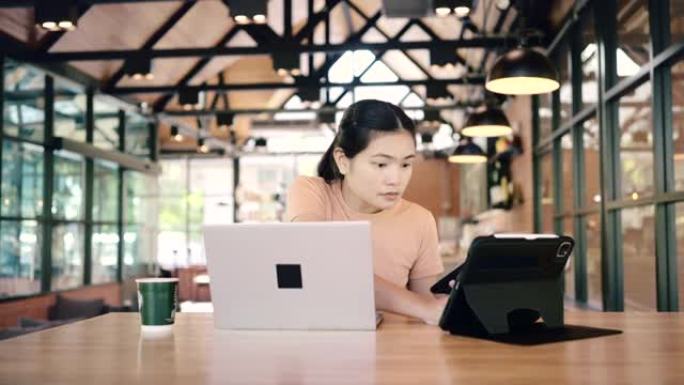 亚洲女性使用笔记本电脑，智能手机，平板电脑交易加密货币在咖啡馆。