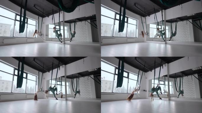 两名年轻的瑜伽士妇女在健身俱乐部的绿色吊床上进行空中瑜伽练习。美丽的女性在课堂上锻炼，表演航空瑜伽。