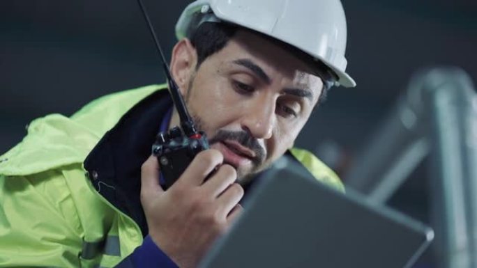 一名男性工人手持数字平板电脑在对讲机上交谈