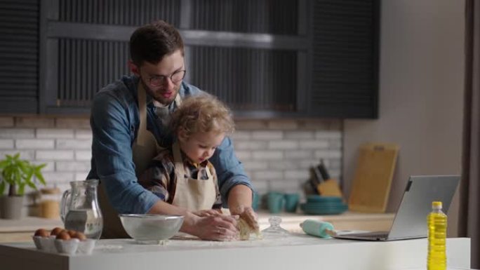小男孩和他的父亲在家里一起煮面包，在餐桌厨房上揉面团，中等肖像