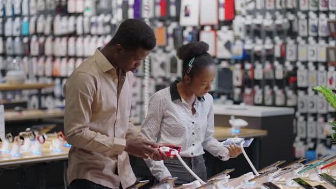 美国黑人已婚夫妇正在数字设备商店中选择智能手机，测试展览样品并讨论模型