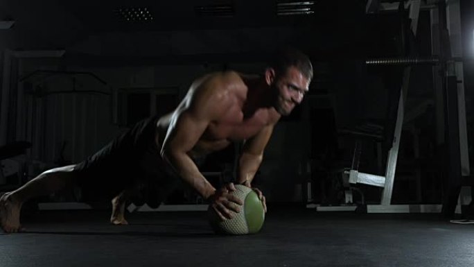 年轻的肌肉发达的人在健身房用球做体操