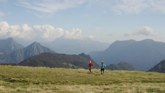 一对夫妇沿着草木山顶徒步旅行的空中无人机拍摄