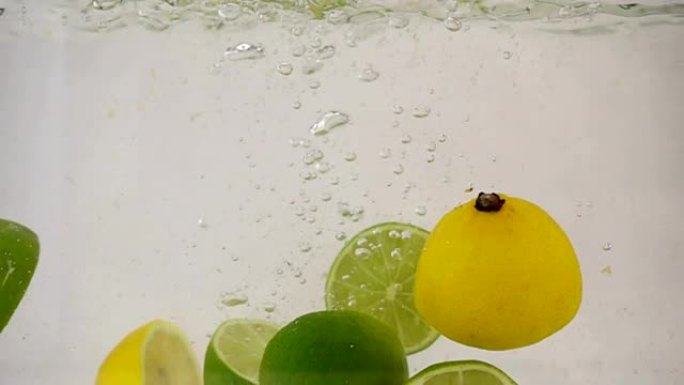 石灰和柠檬的一半落入水中，并带有气泡并喷洒慢动作特写