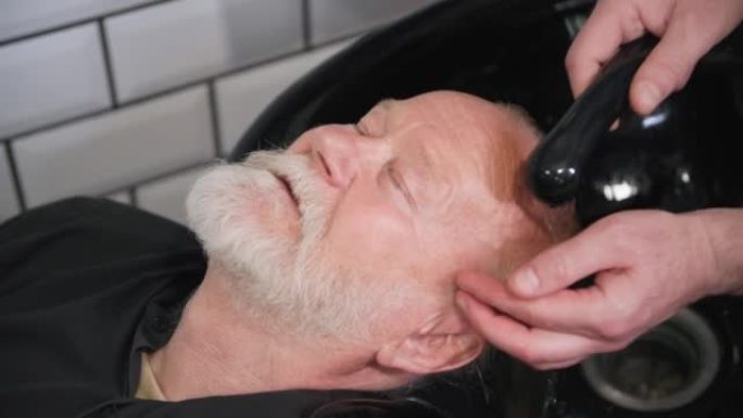 理发店，理发师在理发店洗发前为一位老年顾客洗头