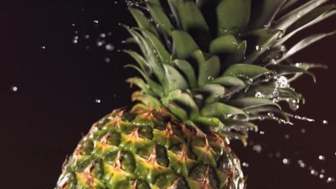超级慢动作水滴在旋转菠萝上。在黑色背景上。
