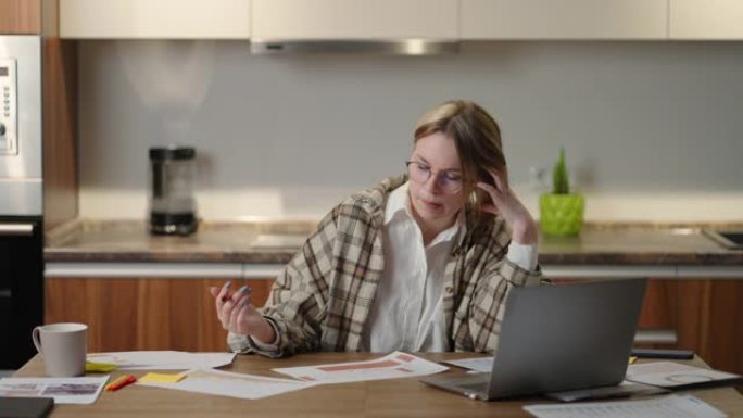 沉思一个戴着眼镜的女人，正在处理财务文件，坐在工作场所使用笔记本电脑应用程序，看上去专注，完成任务，
