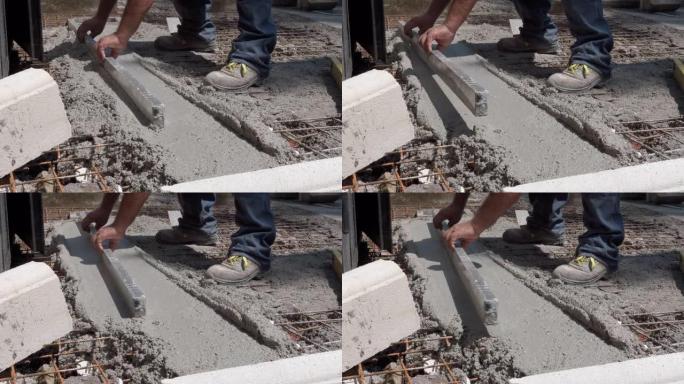 专业建筑承包商在肮脏的衣服和靴子中使用金属调平工具在施工现场对齐或平滑新鲜水泥表面，用湿混凝土熨平板