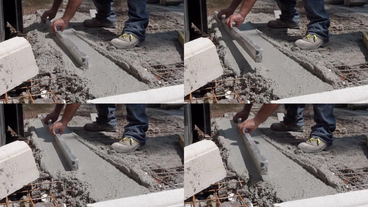 专业建筑承包商在肮脏的衣服和靴子中使用金属调平工具在施工现场对齐或平滑新鲜水泥表面，用湿混凝土熨平板