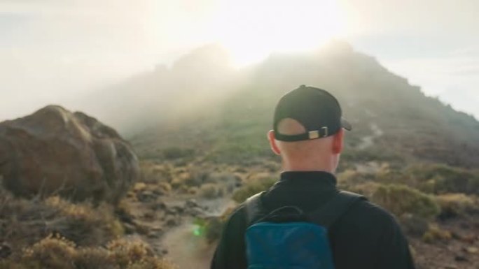 男子走在山上的一条小路上，后视。火山景观