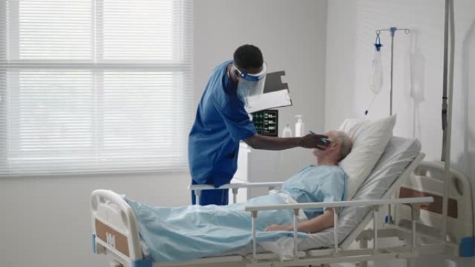 一名老年男性患者躺在医院病床上，与心电图机相连，戴着防护面罩与黑人医生交谈