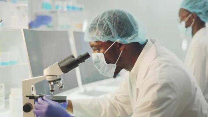 带有显微镜的非洲民族科学家。穿着防护工作服，研究生物有害样品
