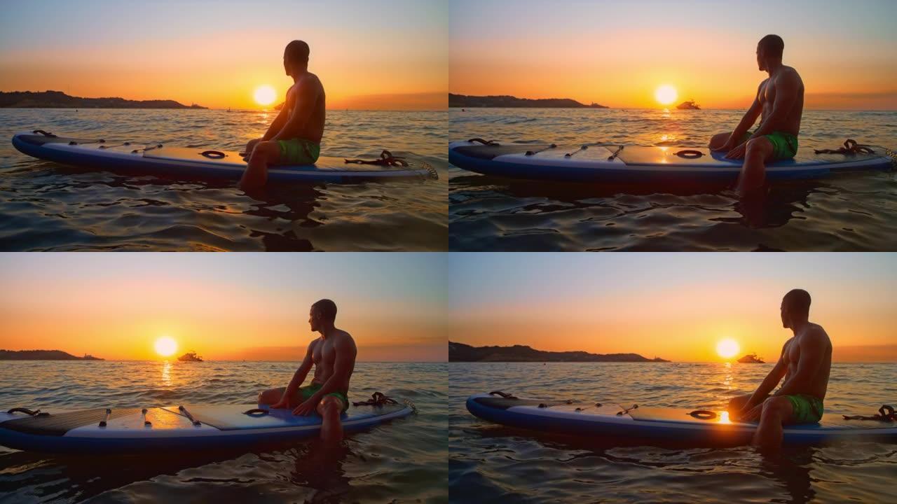 SLO MO Man坐在海上的桨板上观看日落