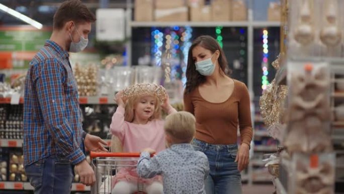 冠状病毒疫情中，一对带着两个孩子的已婚夫妇在购物中心戴着防护口罩，正在为圣诞节做准备，并选择装饰品