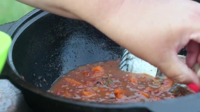 一个女人把鲭鱼放在装有蔬菜的铸铁大锅中。在户外准备食物。特写。