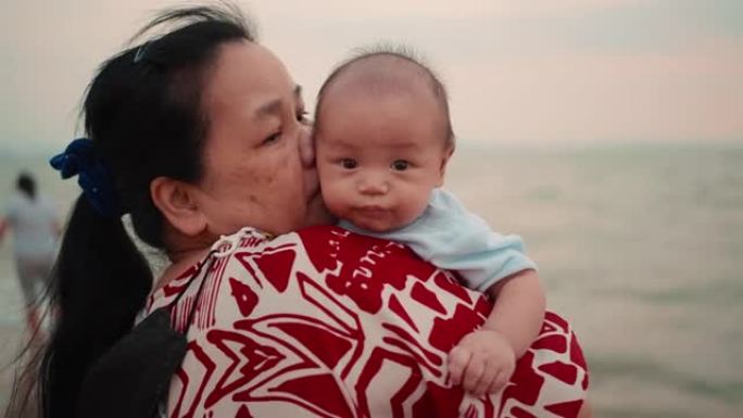 快乐的亚洲祖母抱着她的孙子在海滩上