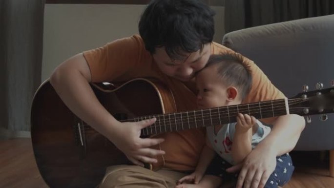 父亲和他蹒跚学步的男孩在家里的客厅弹吉他
