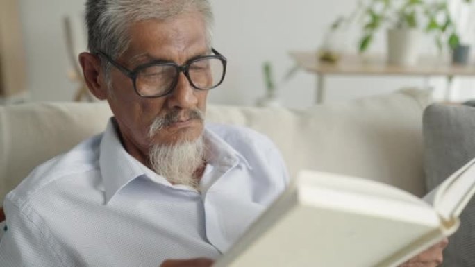 亚洲老年男性白发老人早上在家坐在沙发上看书，爱书人