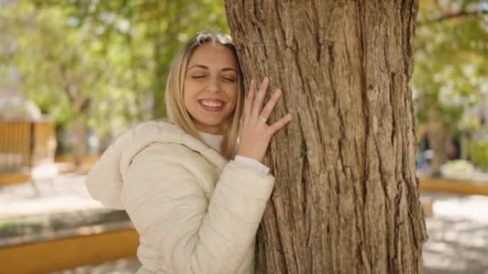 年轻女子微笑着在公园里拥抱树