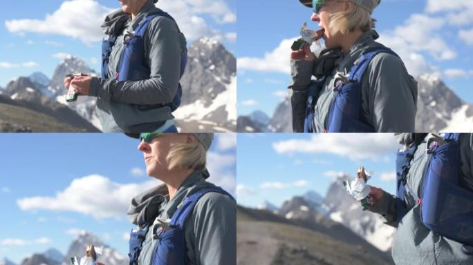 女徒步旅行者在山顶上吃零食，拉焦点