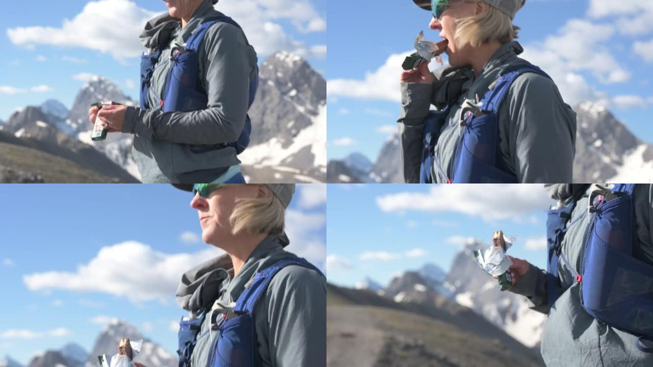 女徒步旅行者在山顶上吃零食，拉焦点
