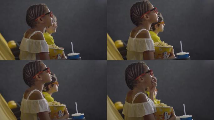小女孩在电影院看3d电影的侧视图，背景模糊的孩子。戴着爆米花的3d眼镜的非洲裔美国孩子在看电影时会产