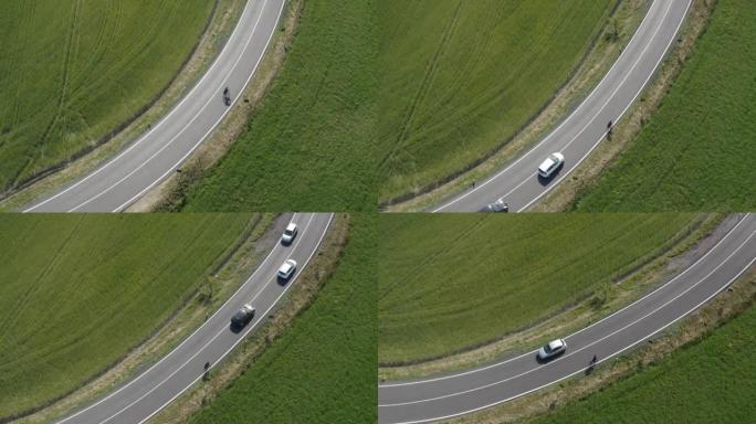 男子在托斯卡纳铺成的道路上骑自行车的空中无人机视图，汽车超越了他