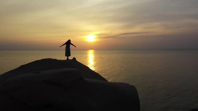 在海滩日落时间站在石头上向前飞行的女人