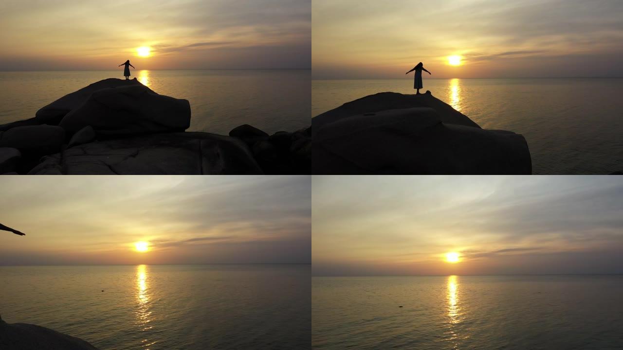 在海滩日落时间站在石头上向前飞行的女人
