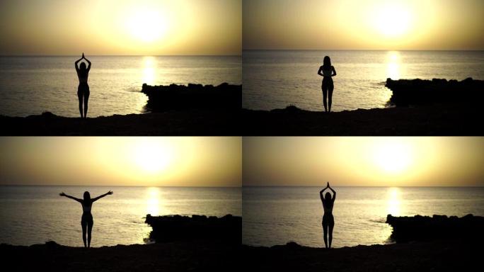 日落映衬的海滩附近练习瑜伽的年轻女子