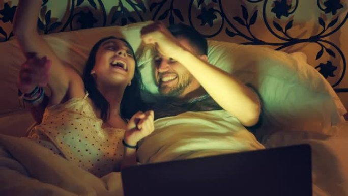 年轻夫妇在床上看恐怖电影。使用笔记本电脑并感到害怕
