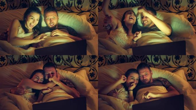 年轻夫妇在床上看恐怖电影。使用笔记本电脑并感到害怕