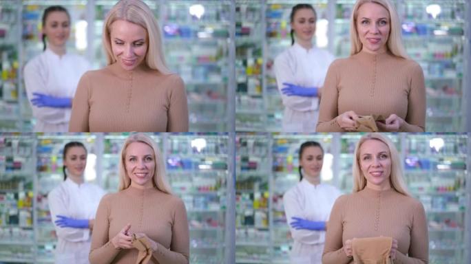 满意的女性客户的肖像在药房里与支撑长袜合影，背景模糊。前视图快乐微笑的白人妇女看着相机广告紧身衣。