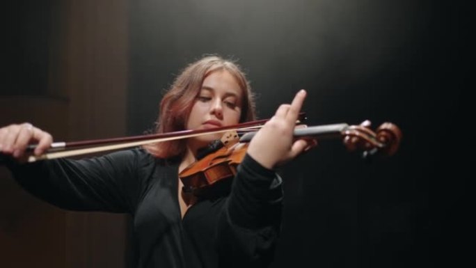 受启发的女小提琴家在音乐学校或黑暗音乐厅演奏小提琴，音乐家演奏经典