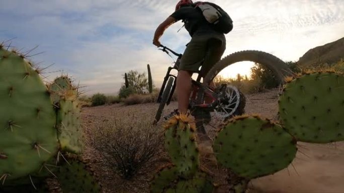 男性山地自行车手在日出时刹车alongs沙漠小径