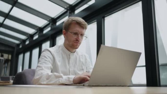 商人在他的现代办公室里使用笔记本电脑，通过互联网发送电子邮件，忙碌而认真的人正在打字