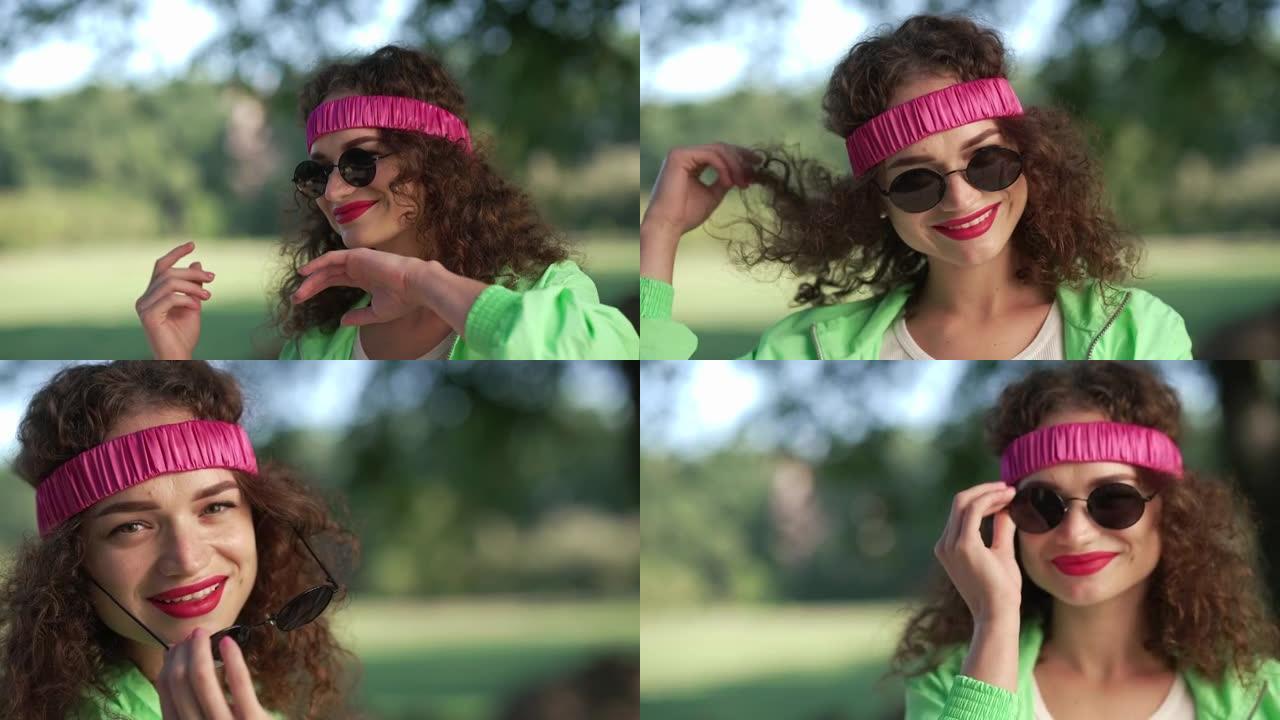快乐自信的女人在夏日公园跳舞，放下墨镜眨眼。调情风趣的黑发卷发高加索复古女士在发带摆姿势在户外玩得开