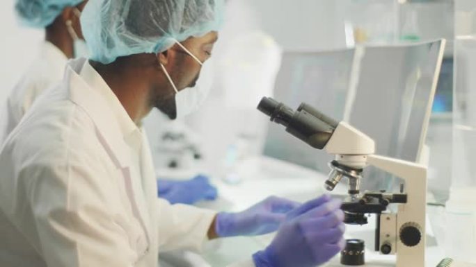 带有显微镜的非洲民族科学家。穿着防护工作服，研究生物有害样品