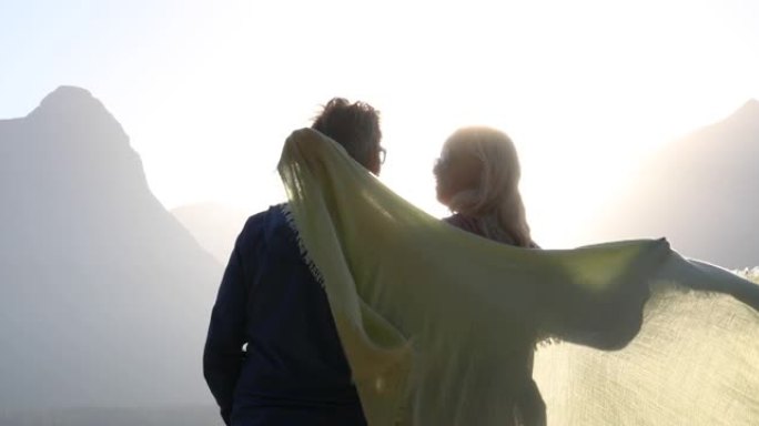 成熟的夫妇在披肩下停下来看日落，遥远的山脉