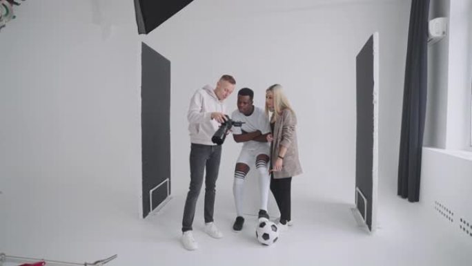 摄影师，足球运动员，模特和导演在相机上观看广告杂志封面的照片