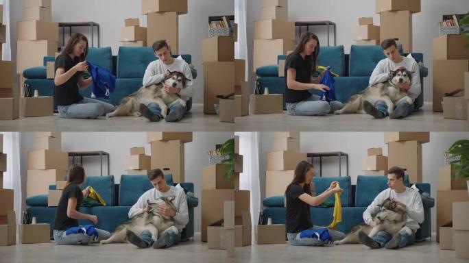 人们生活的新阶段。一个人坐在地板上，抚摸着他心爱的狗。一位朋友坐在附近，折叠衣服以搬到新家。